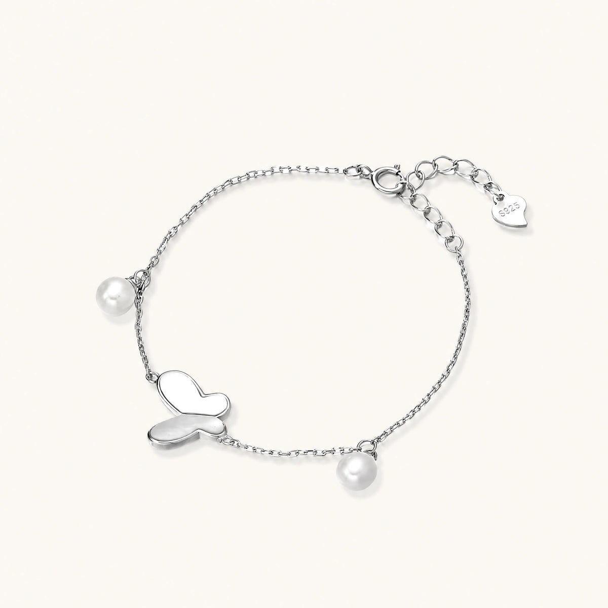 Delicate rhodium-plated silver chain bracelet with butterfly charm and two freshwater pearls on cream background