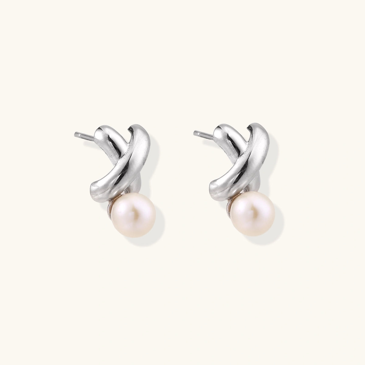 Rhodium-plated silver earrings with twisted X design and freshwater pearl drops on beige background