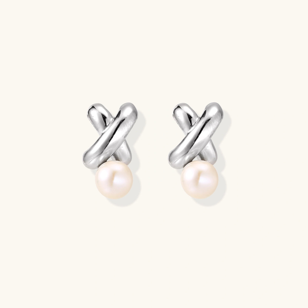 Rhodium-plated silver earrings with twisted X design and freshwater pearl drops on beige background